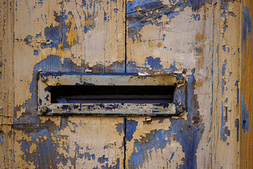 Closeup image of a weathered, peeling paint on an old wooden door with a vintage mail slot, perfect for backgrounds, textures, and rustic-themed designs. Copy space
