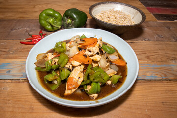 A delicious bowl of Chicken with Green pepper Stir Fry with white rice and peppers with chillies on a wooden kitchen table