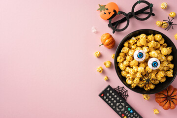 Halloween themed popcorn bowl with candy eyeballs, remote control, and other spooky decorations on...