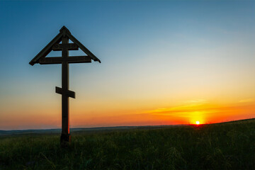 Wooden cross on the meadow at sunset.