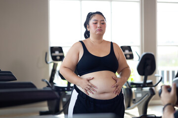 Fototapeta premium Portrait woman and fat belly. beautiful young chubby overweight woman wearing sporty fitness clothes doing exercise indoors at gym fitness sport club, body and health care