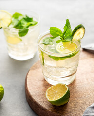 Two glasses lime mojito with mint and ice on a wooden board. Refreshing citrus cocktail on a light background.