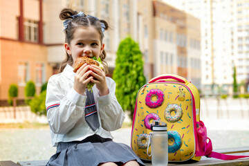school meals, a schoolboy girl has lunch on the street with a hamburger, a child eats a sandwich before school, a schoolboy's fast food