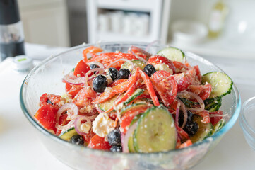 Homemade fresh prepared greek salad with red peppers, cucumber, onions, black olives, tomatoes and feta cheese in a bowl