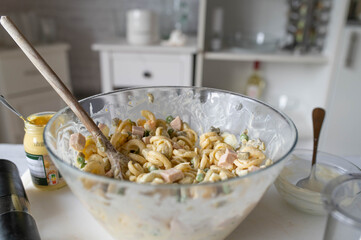 Traditional german pasta salad fresh prepared in the kitchen with mayonnaise, pickles, sausage, green peas and eggs in a bowl