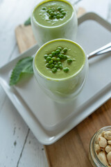 Vegetarian green pea soup fresh and homemade cooked. Served cold for delicious summer meal in glasses on kitchen counter