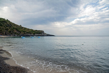 Promontory and beach of the bay with some pedal boats moored. Marina di Camerota, Salerno, Italy.