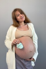 beautiful pregnant woman holding her future baby's booties with her big belly in the background