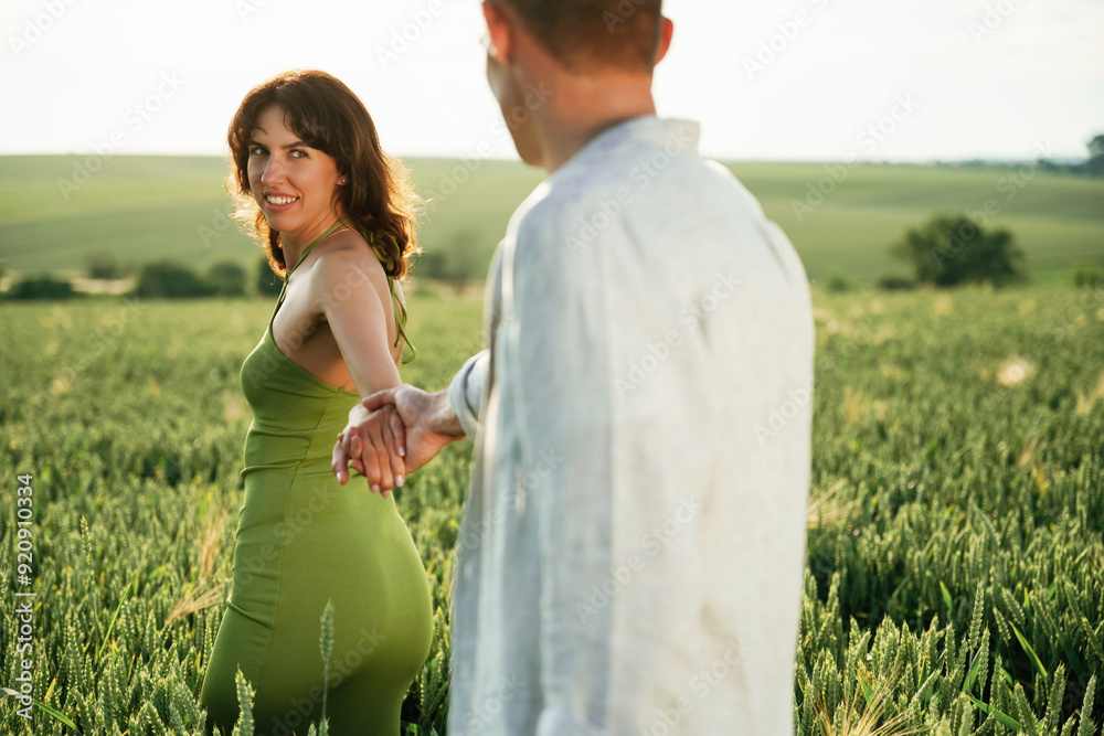 Wall mural Woman is leading the man by a hand. Lovely couple are on the agricultural field together