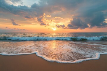 A gentle wave rolls onto a sandy beach at sunset, with a clear blue sky and fluffy clouds.