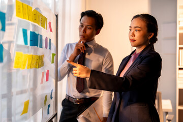 Two people are pointing at a white board with colorful sticky notes on it