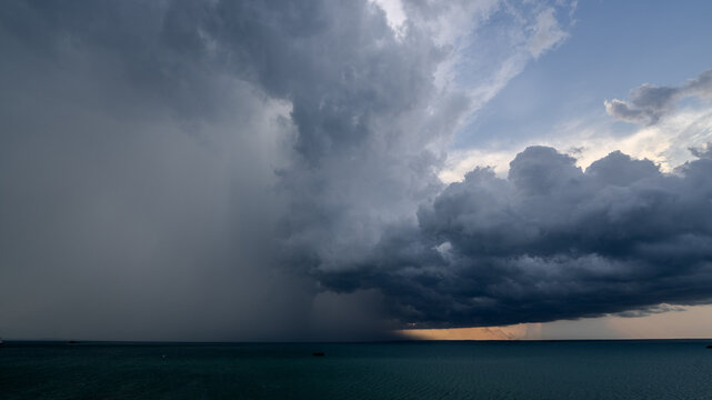 Storm clouds gathering over the ocean with rain visible in the distance. Dramatic sky meets calm waters as a storm approaches the horizon. Concept of Storm, Weather, Ocean, Clouds, Dramatic - Powered by Adobe