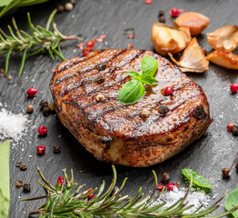 Grilled delicious ribeye steak and some seasonings and herbs on black slate serving plate. Flat lay.