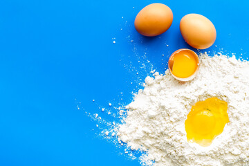 Making dough concept. Pile of flour and eggs on blue background top view copy space