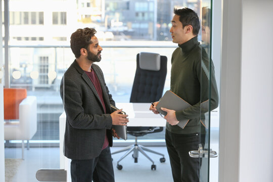 Businessmen talking in office; Two businessmen standing and talking in modern office