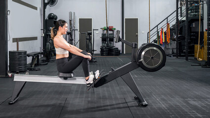 An athletic woman in sportswear is engaged in an intense workout session on a rowing machine inside a well-equipped gym. Health and active lifestyle concept
