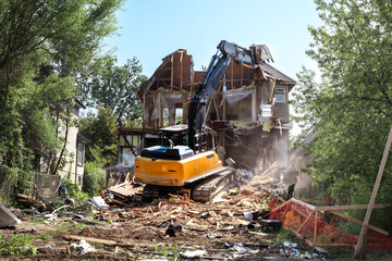 Excavator demolishing house. Large yellow bulldozer on top of building rubbish tearing down roof of...