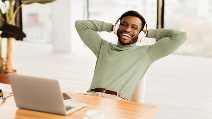 Break At Work. Happy afro businessman listening to music, leaning back in office. Panorama, free space