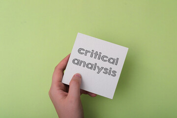 A hand holding a white card with the word critical analysis written on it