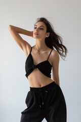Fototapeta premium A woman in black clothing poses for a photo. She is wearing a black top with a tie around her waist and black pants. The photo is in black and white and has a moody, dramatic feel to it