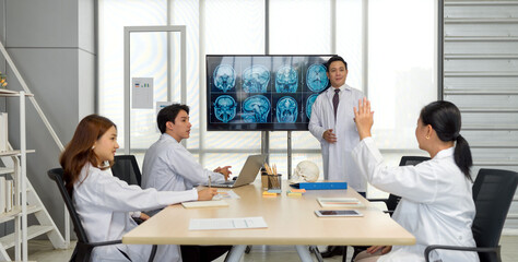 Group of doctor in white gown, discussing brain scan on large monitor in a meeting room.