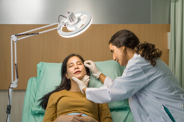 Female doctor or dermatologist examining facial skin of young patient prepare before facelift surgery. Atmosphere at cosmetic surgery department in hospital clinic.