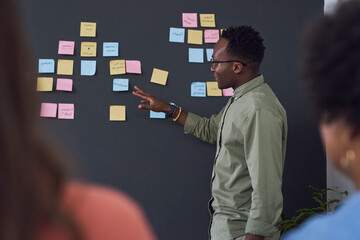 Black man, coach and blackboard with sticky notes in office for training, teaching and learning for...