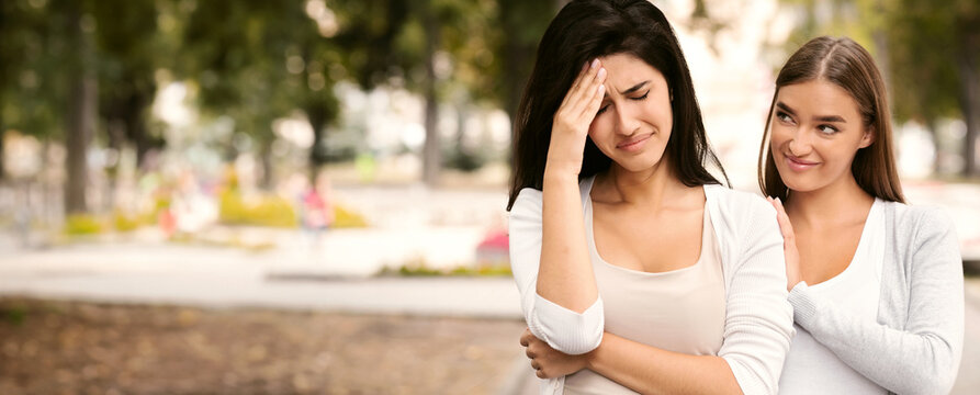 Fake Friendship Concept. Gloating Girl Rejoicing At The Misfortune Of Crying Female Friend Standing Outdoors.