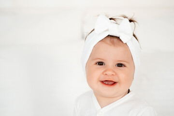 portrait of a smiling little child or baby girl in a white bodysuit on the bed rejoicing, healthy happy baby in the bedroom, space for text