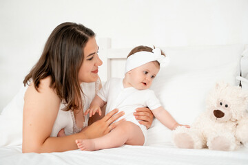 A mother with a small child or infant plays on the bed at home or puts the baby to bed. Happy maternity leave, mom's love and care