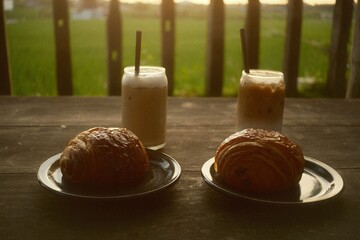 enjoying a plate of pain au chocolat accompanied by an iced coffee latte at the edge of a rice field during sunset