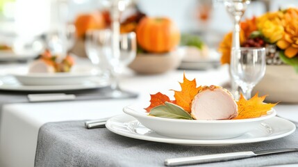 Elegant autumn-themed table setting with white plates, gray napkins, and vibrant fall leaves, ready for a festive celebration.