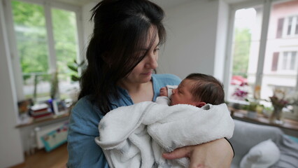 Mother cradling her newborn baby wrapped in a soft white blanket. The tender moment captures the love and bond between mother and child in a cozy home environment