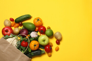 Delivery of vegetarian products. Paper bag with different vegetables and fruits on yellow background, top view. Space for text