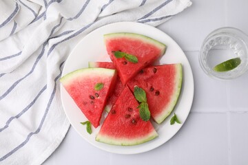 Fresh watermelon slices with mint leaves and glass of water on white tiled table, flat lay