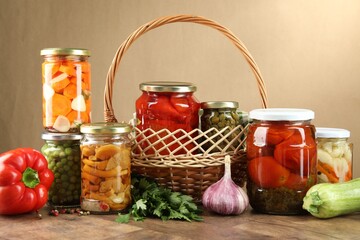 Different pickled products in jars and fresh ingredients on wooden table