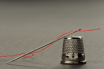 Sewing needle with red thread and thimble on grey background, closeup. Space for text