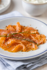 Close-up of Smoked Salmon Slices Garnished with Fresh Herbs and Spices on a White Plate