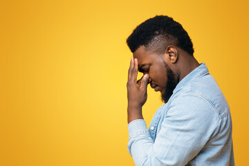 Problems concept. Depressed african american man touching his forehead deep in thoughts, trying to...