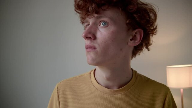 Chest up shot of confused Caucasian guy in plain t-shirt touching face and looking at his hands, looking around room and feeling anxious, experiencing depersonalization-derealization disorder indoors