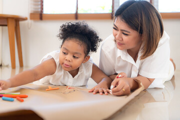 On a holiday, A woman and her little daughters sit on the floor and drawing together in the living room