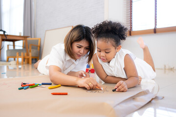 On a holiday, A woman and her little daughters sit on the floor and drawing together in the living room