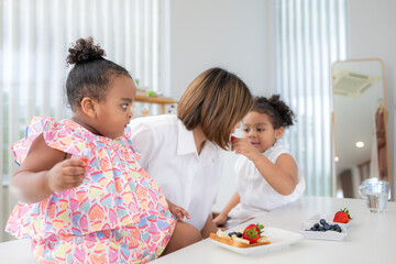 On a holiday, A woman and her two little girls sit in a house's living room and eat fruit