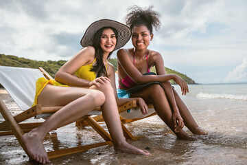 Obraz premium Two women sitting on a beach chair, one wearing a yellow dress