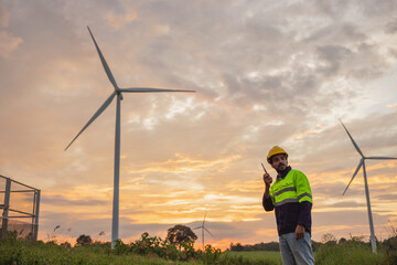 man in a yellow and black safety vest stands in front of two wind turbines