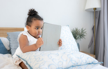 A little girl playing her favorite game on a tablet in the bedroom of the house