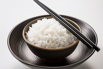Steamed rice is served in a black ceramic Japanese bowl with a pair of chopsticks on top white black ground  
