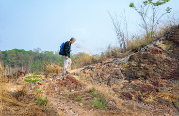 Fototapeta premium healthy senior man in checkered shirt,having a camera,carry backpack climbing on the mountain in the tropical,elderly activity,healthy lifestyle,travel,hiking,adventure in nature