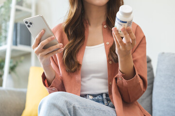 Health care asian young woman using smart phone for reading, searching prescription on bottle medicine, pill label text about information online, instructions side effects, pharmacy medicament concept