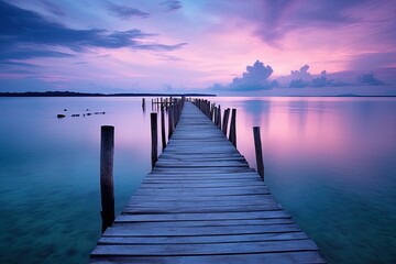 Obraz premium A serene wooden pier extending into calm waters under a colorful sunset sky.